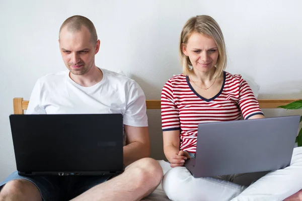 young family works remotely from home on bed at the computer. Quarantined couple coronavirus. Stay home safe. Distance learning, education and work. Order food products online