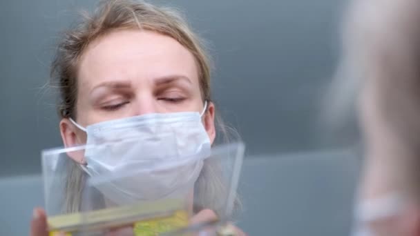 4kだ。医療保護マスクのブロンドの女の子は、アイメイクを行い、アイシャドウを適用します。ミラウを見て。風邪の一般的なインフルエンザに対する女性。隔離室にいて. — ストック動画