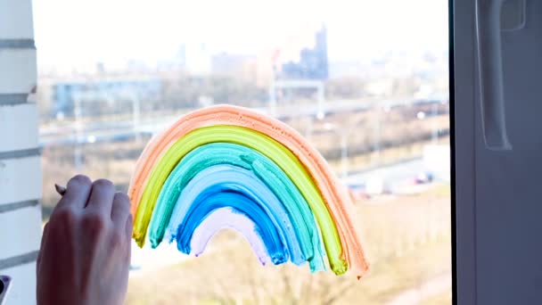 4k. Chica pintando arco iris en la ventana durante la cuarentena Covid-19 en casa. Quédate en casa campaña de medios sociales para la prevención del coronavirus, vamos a estar todos bien, esperanza. Atrapar el arco iris . — Vídeos de Stock