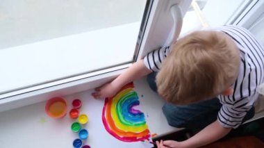 Evde Covid-19 karantinası sırasında gökkuşağını boyayan küçük sarışın çocuk. Coronavirus önleme kampanyası için sosyal medya kampanyasında kalalım. Hepimiz iyi olalım, umut edelim. Gökkuşağını kovala