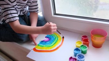 Evde Covid-19 karantinası sırasında gökkuşağını boyayan küçük sarışın çocuk. Coronavirus önleme kampanyası için sosyal medya kampanyasında kalalım. Hepimiz iyi olalım, umut edelim. Gökkuşağını kovala