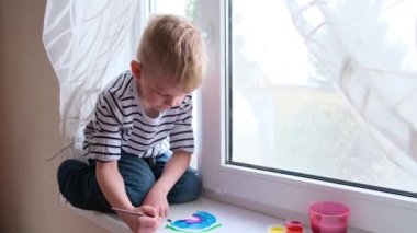 Evde Covid-19 karantinası sırasında gökkuşağını boyayan küçük sarışın çocuk. Coronavirus önleme kampanyası için sosyal medya kampanyasında kalalım. Hepimiz iyi olalım, umut edelim. Gökkuşağını kovala