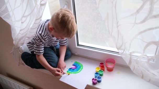 4k.Kleiner blonder Junge beim Bemalen des Regenbogens während der Covid-19 Quarantäne zu Hause. Bleiben Sie zu Hause Social-Media-Kampagne für Coronavirus-Prävention, lassen Sie alles gut sein, hoffen. Jagd auf den Regenbogen — Stockvideo