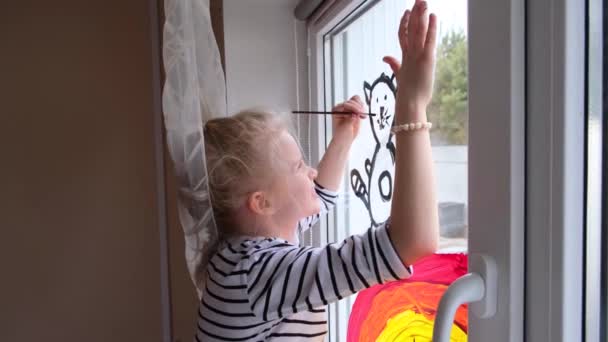 4k. Девушка рисует радугу и кошку на окне во время карантина Ковид-19 дома. Сиди дома. Идея детского дома. Погоня за радугой — стоковое видео