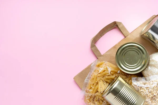 Paper bag with Food supplies crisis food stock for quarantine isolation period on pink. Rice, pasta, oatmeal, canned food, sugar, toilet paper. Food delivery, Donation, coronavirus. Copyspace — Stock Photo, Image