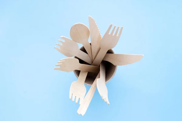 Utensilios de cocina desechables ecológicos sobre fondo azul. tenedores de madera y cucharas en taza de papel. ecología, concepto de cero residuos. Vista superior. plano laico — Foto de Stock