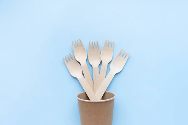 Eco friendly disposable kitchenware utensils on blue background. wooden forks and spoons in paper cup. ecology, zero waste concept. top view. flat lay — Stock Photo, Image