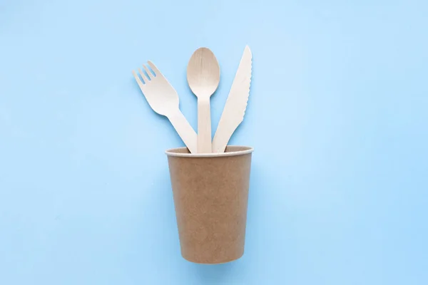 Utensilios de cocina desechables ecológicos sobre fondo azul. tenedores de madera y cucharas en taza de papel. ecología, concepto de cero residuos. Vista superior. plano laico — Foto de Stock