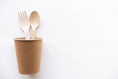 Beyaz arka planda çevre dostu tek kullanımlık mutfak gereçleri. Kağıt bardakta tahta çatallar ve kaşıklar. Ekoloji, sıfır atık kavramı. Üst Manzara. düz yat