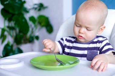 Bebek maması. Küçük, beyaz, kaşık ve boş yeşil tabağı olan bir çocuk. Yeni doğmuş bebekler.