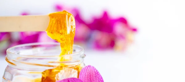 Pasta de azúcar bandera o miel de cera para la eliminación del cabello fluye hacia abajo de palos de espátula de cera de madera. fondo de flores - depilación y concepto de belleza —  Fotos de Stock