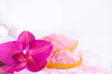 Spa kozmetik ve güzellik tedavi konsepti. Pembe spa deniz tuzu, beyaz havlu ve beyaz ahşap arka planda mor orkide. çoğaltma düzlemi