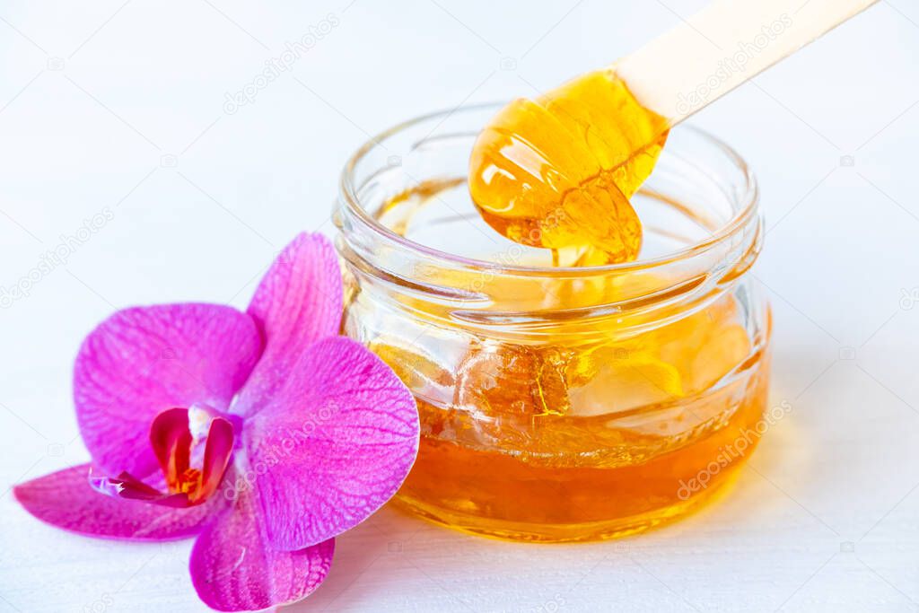 sugar paste or wax honey for hair removing flows down from wooden waxing spatula sticks in jar. flower background - depilation and beauty concept