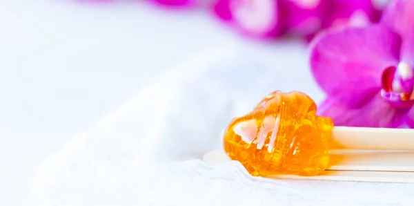 Pasta de azúcar bandera o miel de cera para eliminar el cabello con palos de espátula de cera de madera. fondo de flores - depilación y concepto de belleza —  Fotos de Stock