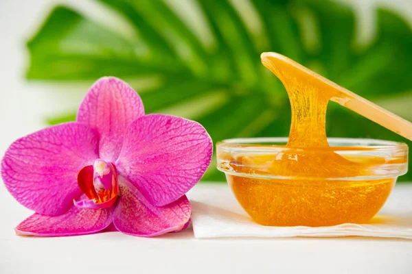 Pasta de azúcar o miel de cera para eliminar el cabello fluye hacia abajo de palitos de espátula de cera de madera. fondo de flores - depilación y concepto de belleza —  Fotos de Stock