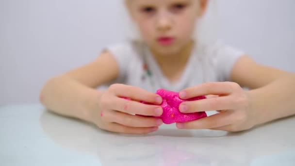 Blondes Mädchen, das rosa Glitzerschleim an die Seiten streckt. Kinderhände spielen Schleimspielzeug. Schleim machen. Kopierraum. Selektiver Fokus. — Stockvideo