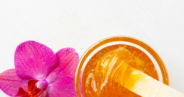 Pasta de azúcar o miel de cera para eliminar el cabello con palitos de espátula de cera de madera. fondo de flores - depilación y concepto de belleza —  Fotos de Stock