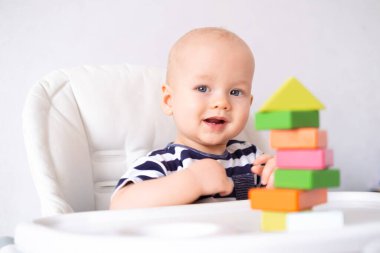 Bebek oyunu. Küçük zeki beyaz çocuk renkli ahşap oyuncaklarla oynuyor. Sandalyede ev ya da küp kulesi yapıyor. Erken gelişim için oyunlar. Yeni doğan çocuklar boş vakit geçirir.
