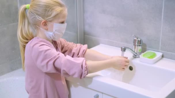 Tıbbi maskeli çocuk sarışın kız modern banyoda ellerini yeşil sabunla yıkıyor. Temizlik, hijyen ve önleme. 4k görüntü — Stok video