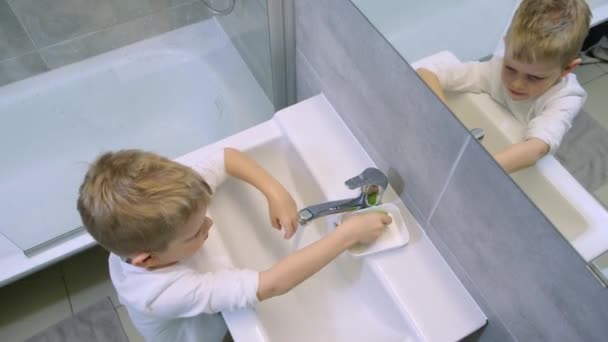 Der kleine blonde Junge wäscht sich im modernen Badezimmer die Hände mit grüner Seife. Reinigung, Hygiene und Prävention. 4k Filmmaterial — Stockvideo