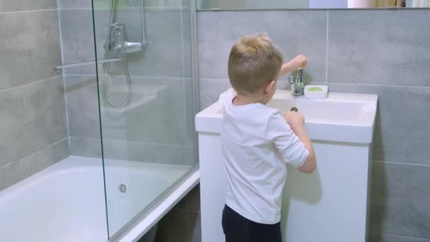 Menino loiro criança está lavando as mãos com sabão verde no banheiro moderno. Limpeza, higiene e prevenção. Filmagem 4k — Vídeo de Stock