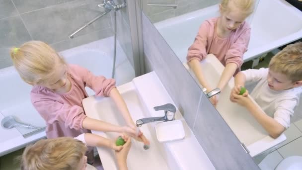 Ragazzo biondo e ragazza in bagno. Bambini lavarsi le mani con sapone verde nel bagno moderno. Pulizia, igiene e prevenzione. 4k filmati — Video Stock