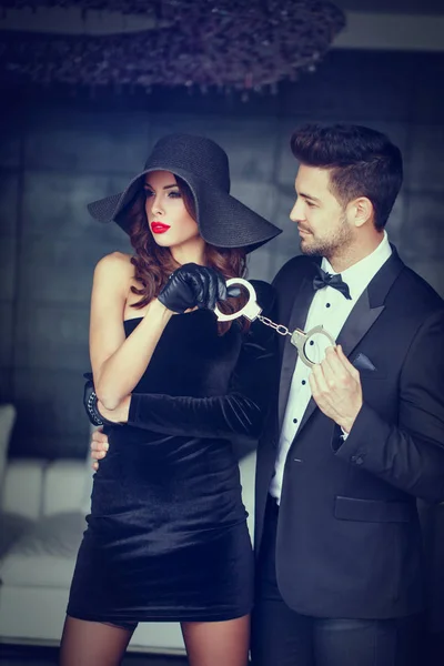 Mujer sexy en sombrero sosteniendo hombre rico en esmoquin en las esposas — Foto de Stock