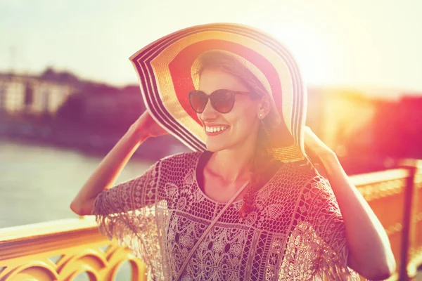 Happy young woman in hat walking on bridge in sunset, positivity — Stock Photo, Image