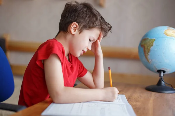 Triste niño trabajando en la tarea en casa solo — Foto de Stock