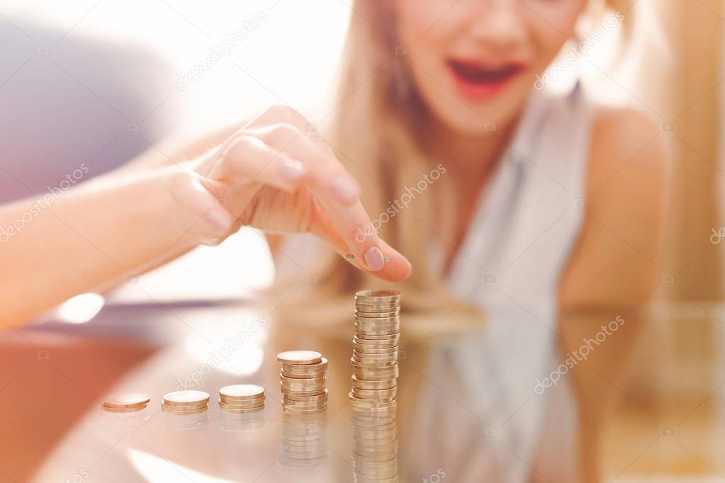Excited young woman building coin columns on glass desk