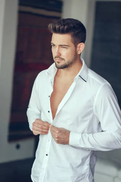 Young rich confident man buttoning shirt indoor — Stock Photo, Image