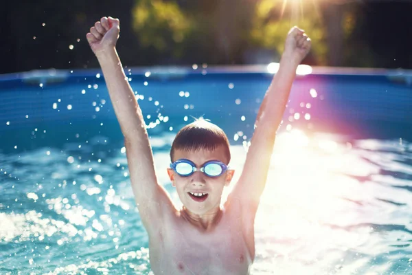 Happy little boy hands up in swimming pool in sunset — Stock Photo, Image