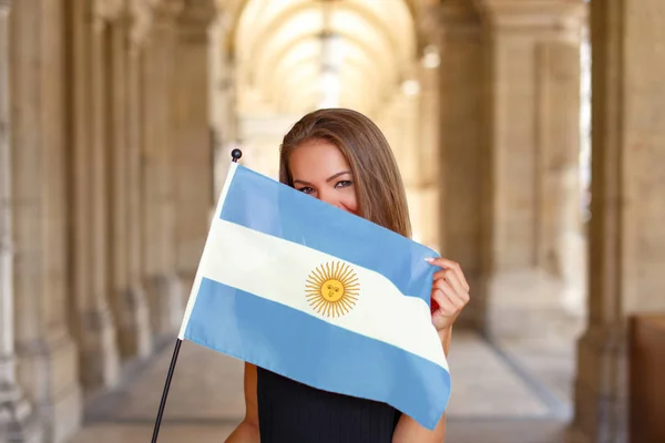 Mujer joven y feliz cubriéndose la cara con la bandera de Argentina —  Fotos de Stock