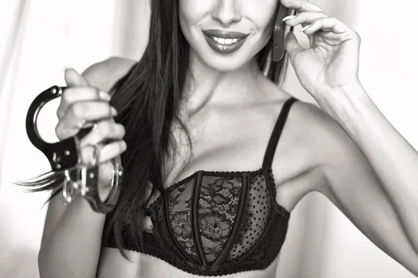 Sexy brunette woman calling and holding handcuffs black and whit — Stock Photo, Image
