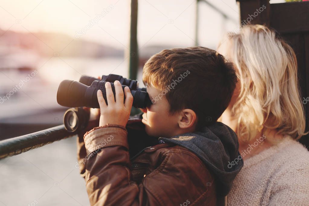 Little boy watching into distantance by binoculars with mother i