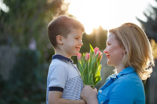 Little son gives bouquet of tulips to mom at Mother\'s day in sun