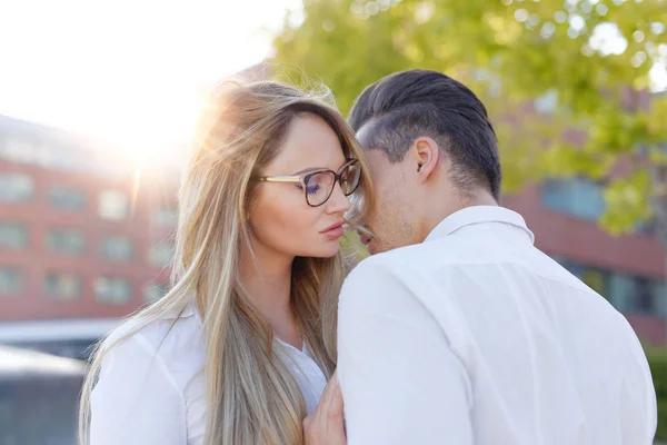Joven mujer rubia susurra al hombre declaración de amor al aire libre — Foto de Stock