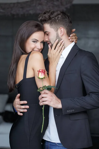 Χαρούμενος νεαρός με τριαντάφυλλο εκμετάλλευση αγκαλιάσει όμορφη γυναίκα εσωτερική — Φωτογραφία Αρχείου