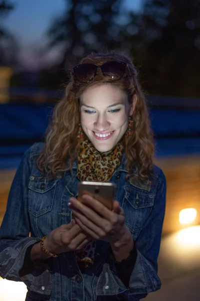 Joyeux jeune femme souriant sur le message la nuit, à l'extérieur — Photo