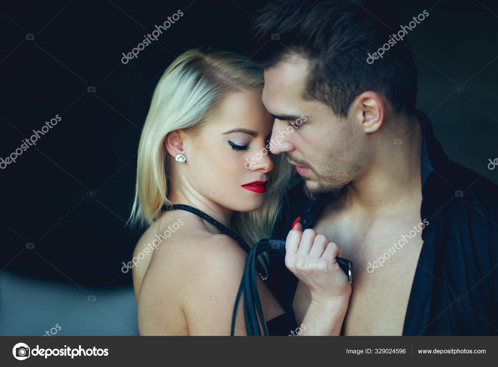 Sexy dominant blonde woman with macho man lover holding whip Stock Photo by ©sakkmesterke 329024596