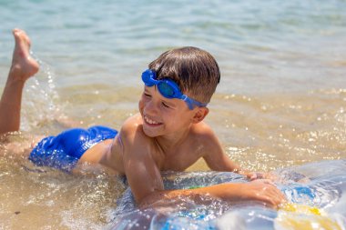 Kumsaldaki deniz suyunda yatan küçük çocuk.