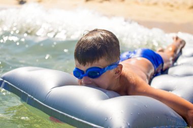 Gözlüklü küçük mutlu çocuk denizdeki şişme su yatağında yatıyor.