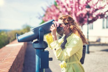 Genç kızıl saçlı turist kadın parkta dürbünle izliyor.