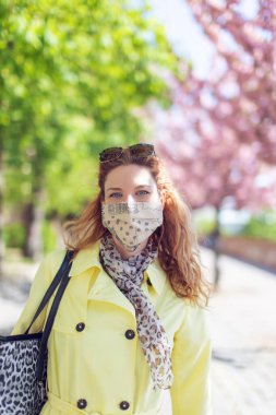 Sarı ceketli ve maskeli kadın salgın sırasında parkta.