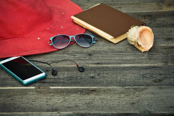 A hat, smartphone, a book as well of wooden background