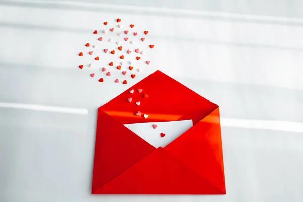 Opened red envelope and many felt hearts on white background with place for text. Love letter mail correspondence relationship. Valentines day concept. Top view. Copy space.