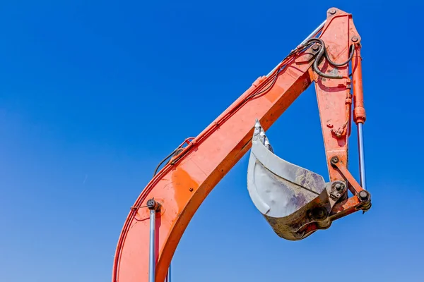 Graafmachine van hulpmiddel, emmer, blade, verhoogd van de arm, blauwe hemel achter — Stockfoto