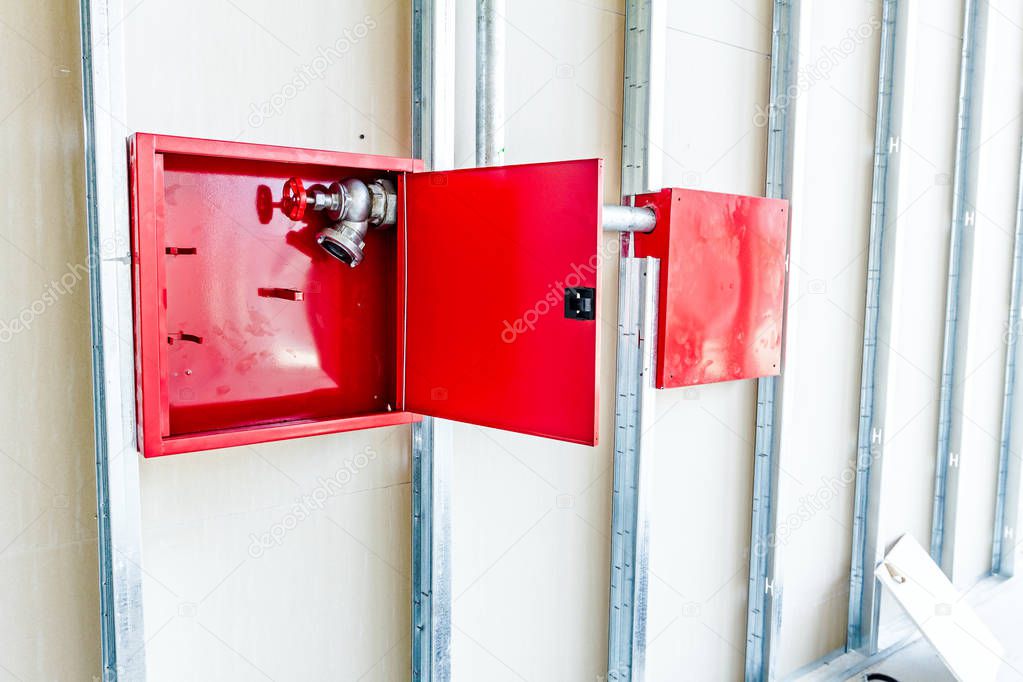 Red box with fire hydrant is built in an unfinished plaster wall