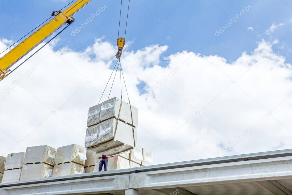 Mobile crane is raising package of glass wool on the roof huge u