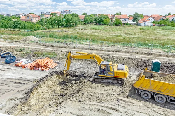 Grävmaskin gräva ett dike och lastning en lastbil på bygga si — Stockfoto